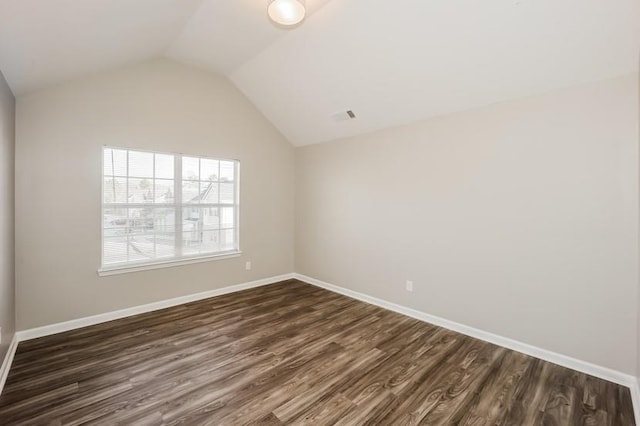 empty room featuring dark wood-style floors, visible vents, vaulted ceiling, and baseboards