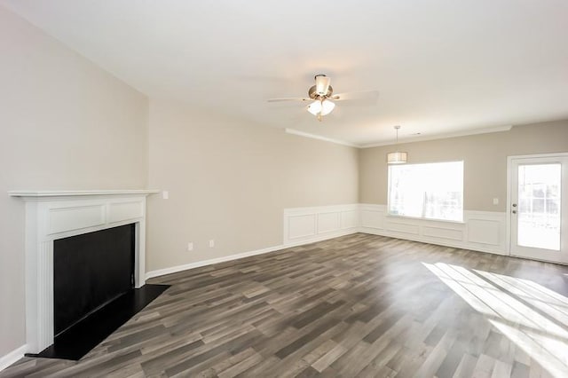 unfurnished living room featuring a decorative wall, a fireplace, a ceiling fan, wainscoting, and dark wood-style floors