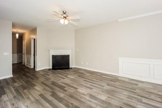 unfurnished living room featuring ceiling fan, a decorative wall, a wainscoted wall, a fireplace with flush hearth, and dark wood-style floors