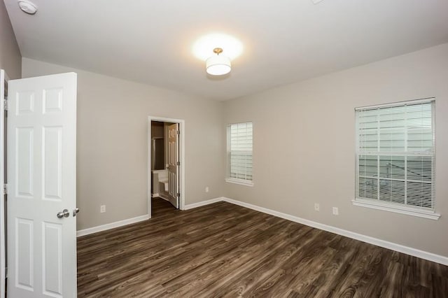 unfurnished bedroom with dark wood-style floors, ensuite bath, and baseboards