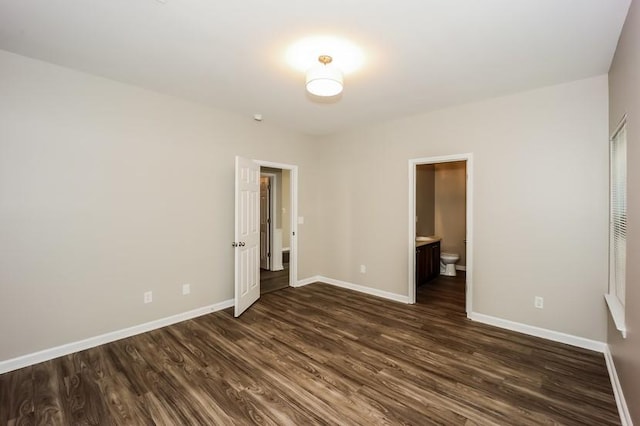 unfurnished bedroom with ensuite bath, baseboards, and dark wood finished floors