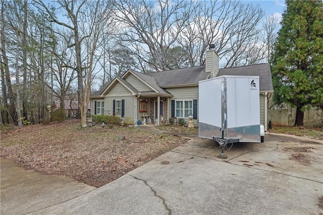 view of front of house with concrete driveway, fence, and a chimney