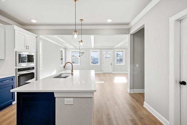 kitchen featuring decorative light fixtures, a center island with sink, sink, appliances with stainless steel finishes, and white cabinets