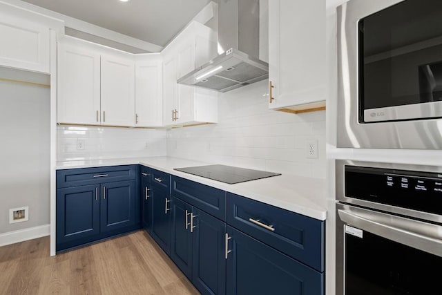 kitchen with tasteful backsplash, wall chimney range hood, stainless steel appliances, white cabinets, and blue cabinets