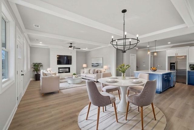 dining space featuring a fireplace, beam ceiling, sink, light hardwood / wood-style flooring, and ceiling fan with notable chandelier