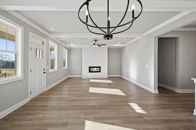 unfurnished living room featuring wood-type flooring, a fireplace, ceiling fan with notable chandelier, and ornamental molding