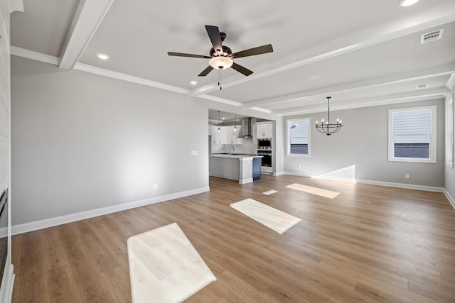 unfurnished living room with sink, beamed ceiling, ceiling fan with notable chandelier, and light hardwood / wood-style flooring