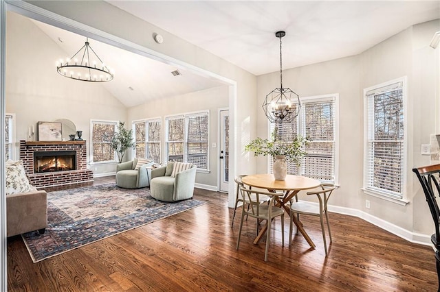 dining space featuring a brick fireplace, an inviting chandelier, and wood finished floors