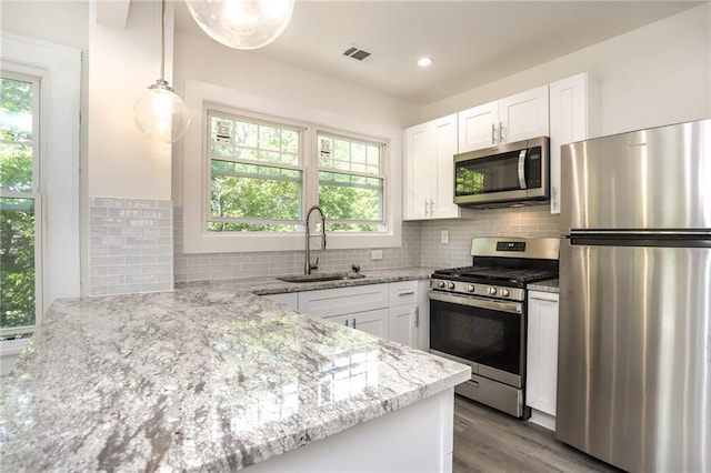 kitchen featuring white cabinets, appliances with stainless steel finishes, light stone countertops, decorative light fixtures, and sink