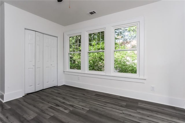 unfurnished bedroom with multiple windows, dark hardwood / wood-style floors, and a closet