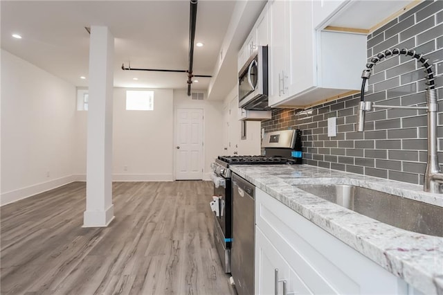 kitchen featuring white cabinets, appliances with stainless steel finishes, light stone countertops, light wood-type flooring, and sink