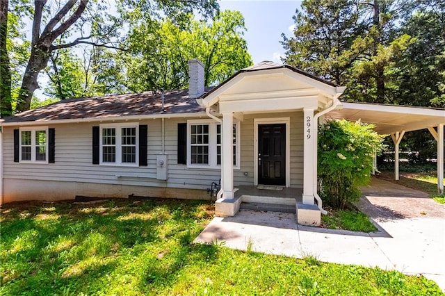 view of front of home with a carport, a chimney, and a front yard