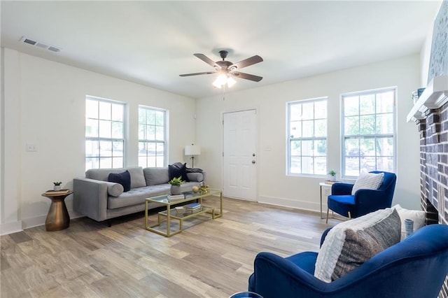 living room with visible vents, a brick fireplace, a ceiling fan, and light wood-style floors