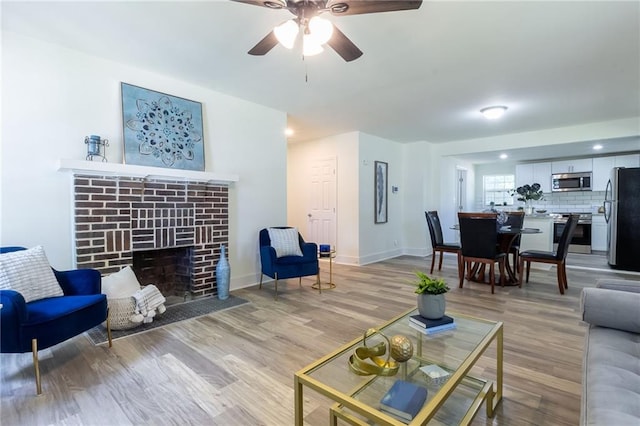 living area with a fireplace, a ceiling fan, light wood-style floors, and baseboards