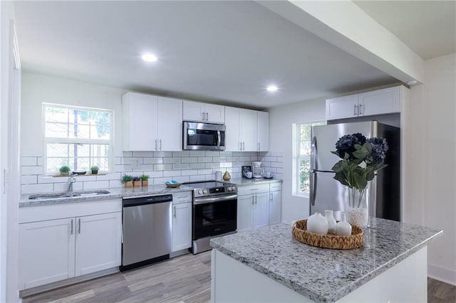kitchen featuring backsplash, light wood-style floors, white cabinets, stainless steel appliances, and a sink