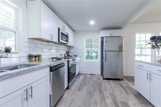 kitchen with light stone countertops, decorative backsplash, appliances with stainless steel finishes, light wood-style floors, and white cabinetry