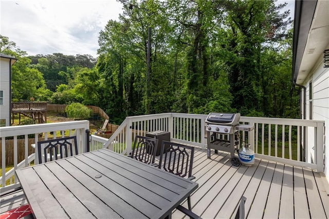 deck featuring outdoor dining area, a wooded view, and area for grilling