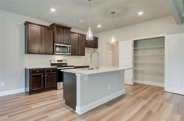 kitchen with decorative light fixtures, sink, light stone counters, stainless steel appliances, and a center island with sink