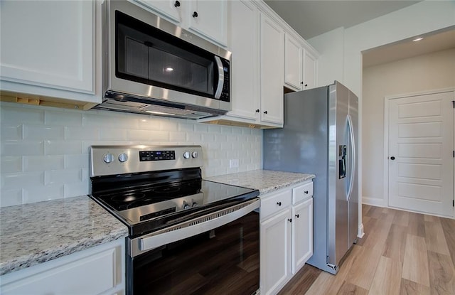 kitchen with white cabinetry, backsplash, stainless steel appliances, light stone countertops, and light wood-type flooring