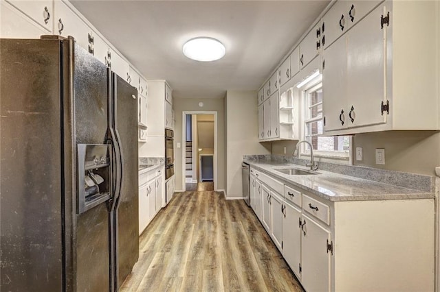 kitchen featuring black appliances, white cabinets, light wood-type flooring, and sink