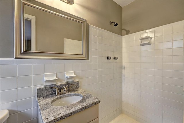 bathroom with a tile shower, vanity, tile walls, and toilet