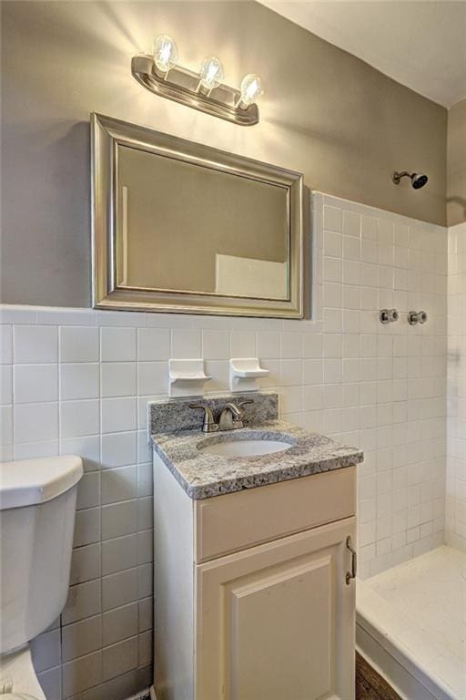 bathroom with a tile shower, vanity, toilet, and tile walls