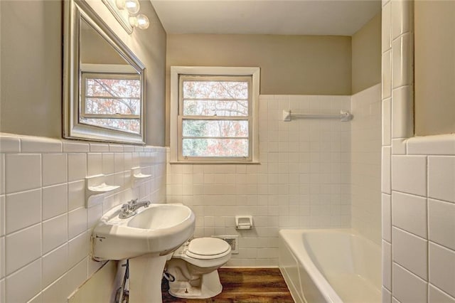 bathroom with hardwood / wood-style flooring, a tub to relax in, toilet, and tile walls