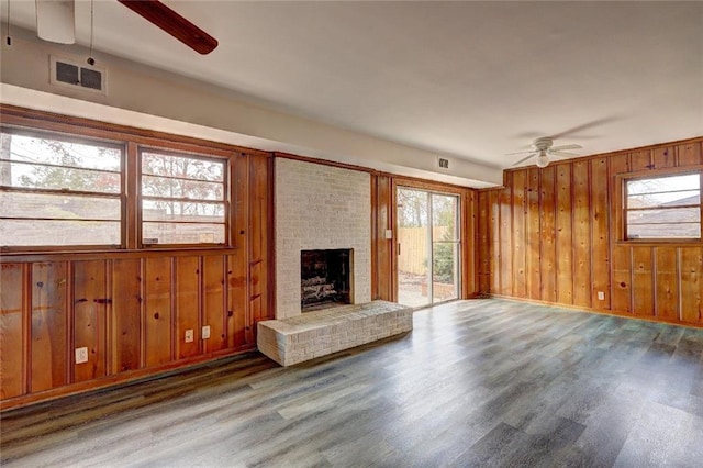 unfurnished living room with hardwood / wood-style floors, ceiling fan, a fireplace, and wooden walls