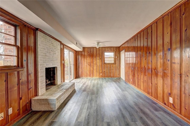 unfurnished living room with ceiling fan, wood walls, dark hardwood / wood-style flooring, and a brick fireplace