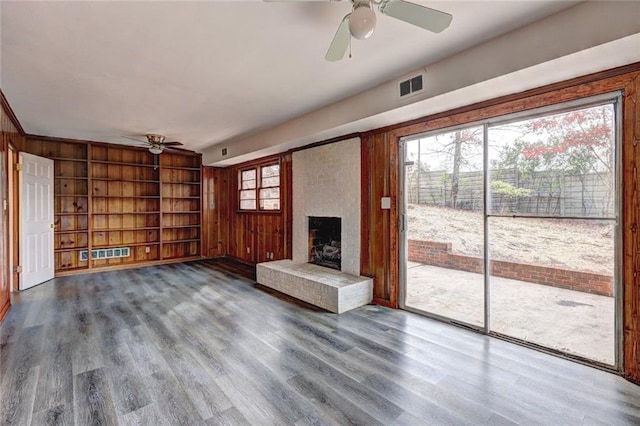 unfurnished living room with hardwood / wood-style floors, a large fireplace, a wealth of natural light, and built in shelves