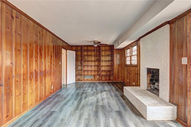 unfurnished living room featuring ceiling fan, a brick fireplace, built in features, wood walls, and light wood-type flooring