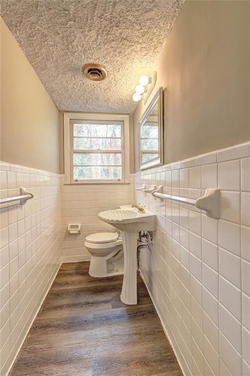 bathroom featuring hardwood / wood-style flooring, toilet, tile walls, and a textured ceiling