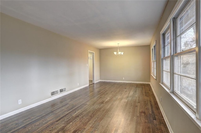 spare room with a chandelier and dark hardwood / wood-style floors