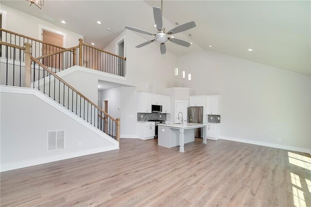 unfurnished living room featuring visible vents, a ceiling fan, light wood-style floors, stairs, and high vaulted ceiling
