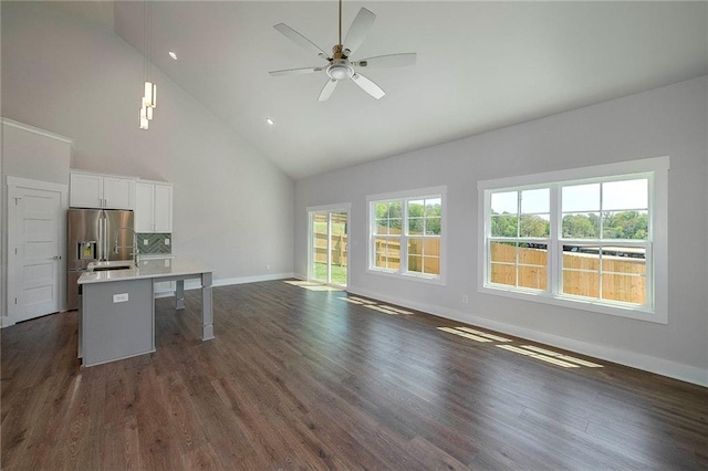 unfurnished living room featuring dark wood-type flooring, ceiling fan, high vaulted ceiling, and baseboards