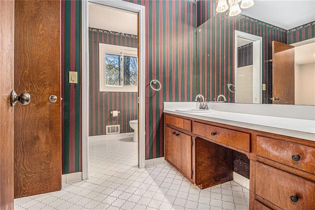 bathroom featuring vanity, visible vents, baseboards, wallpapered walls, and toilet