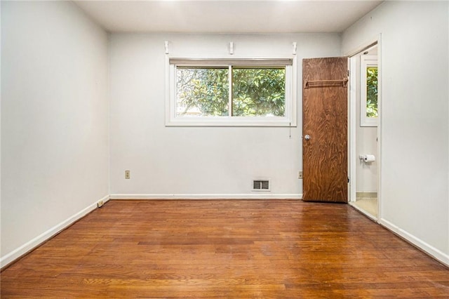 unfurnished room with baseboards, wood finished floors, visible vents, and a healthy amount of sunlight