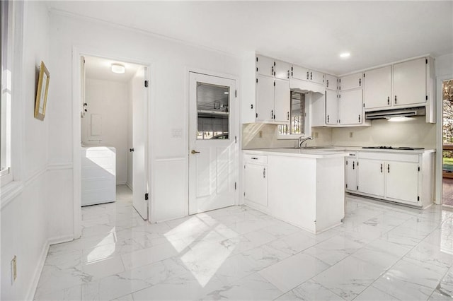 kitchen with crown molding, under cabinet range hood, light countertops, a peninsula, and marble finish floor