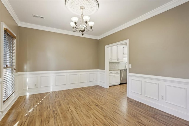 empty room featuring a notable chandelier, ornamental molding, and light hardwood / wood-style flooring