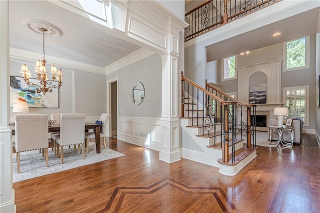 dining room with crown molding, a towering ceiling, dark hardwood / wood-style floors, a notable chandelier, and ornate columns