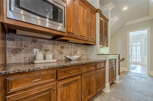 kitchen featuring stainless steel microwave, tasteful backsplash, ornamental molding, and dark stone countertops