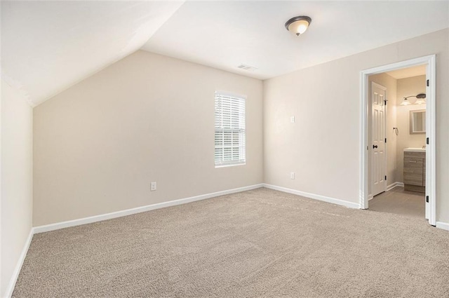 unfurnished bedroom with light colored carpet, lofted ceiling, and ensuite bath