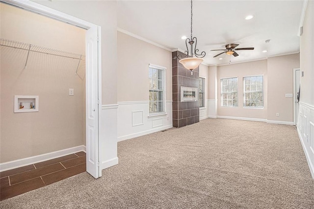 unfurnished living room with a tiled fireplace, ornamental molding, carpet, and ceiling fan