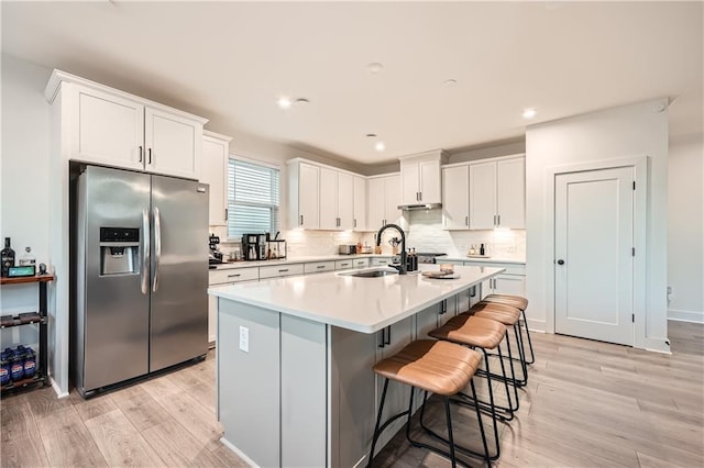 kitchen featuring stainless steel refrigerator with ice dispenser, a sink, backsplash, white cabinetry, and light countertops