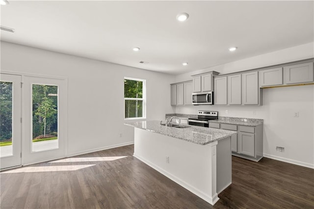 kitchen featuring gray cabinetry, dark wood-type flooring, a center island with sink, light stone counters, and stainless steel appliances