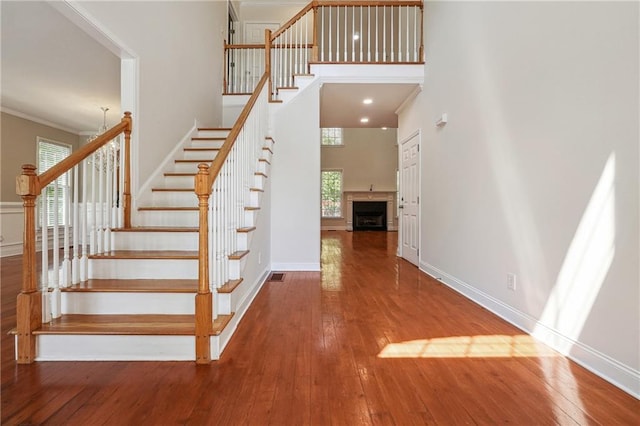 stairway with hardwood / wood-style floors, a towering ceiling, ornamental molding, and visible vents