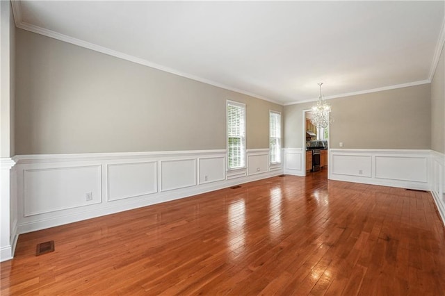 spare room featuring a wainscoted wall, visible vents, ornamental molding, wood-type flooring, and a notable chandelier