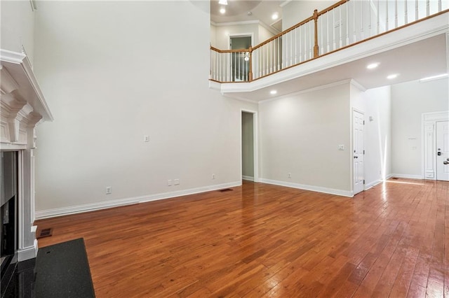 unfurnished living room with hardwood / wood-style floors, a towering ceiling, ornamental molding, baseboards, and a fireplace