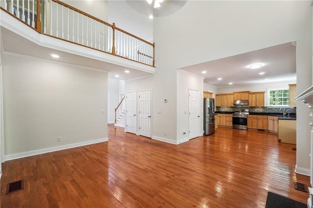unfurnished living room featuring stairway, a towering ceiling, visible vents, dark wood-style flooring, and ceiling fan