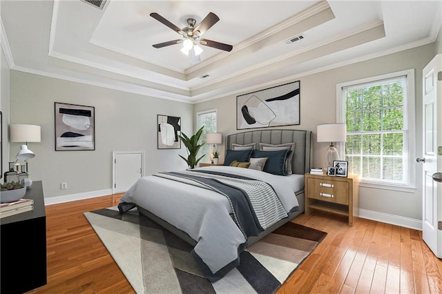 bedroom featuring a tray ceiling, visible vents, ornamental molding, baseboards, and light wood-style flooring
